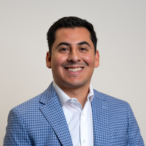 Omar Vazquez, Sport Psychology Postdoc, smiling at the camera while wearing a blue checkered blazer and white shirt.